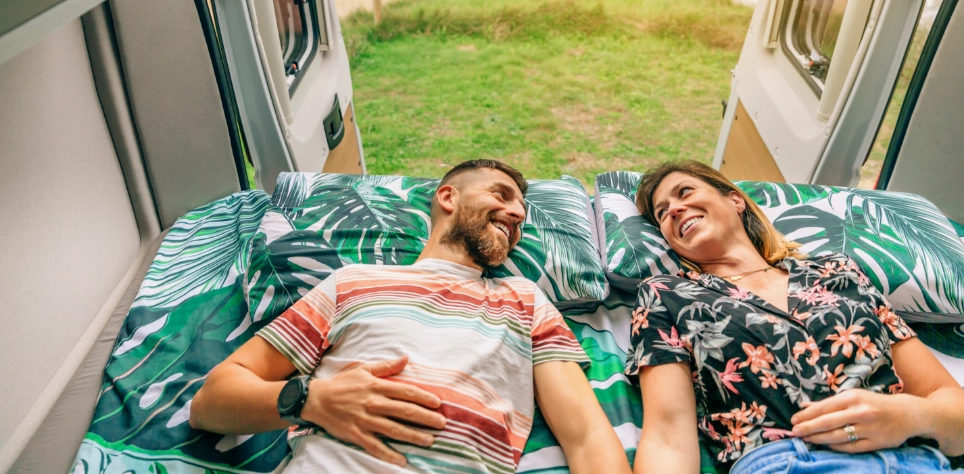 Stel ontspant op bed in camperbus met tropisch beddengoed, vanlife vakantie