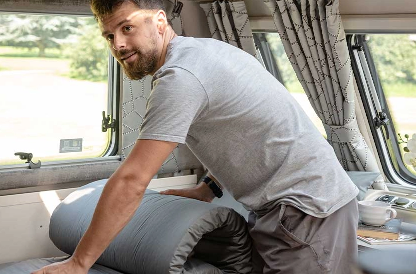 Kampeerder rolt dekbed op in caravan, beddengoed opruimen.